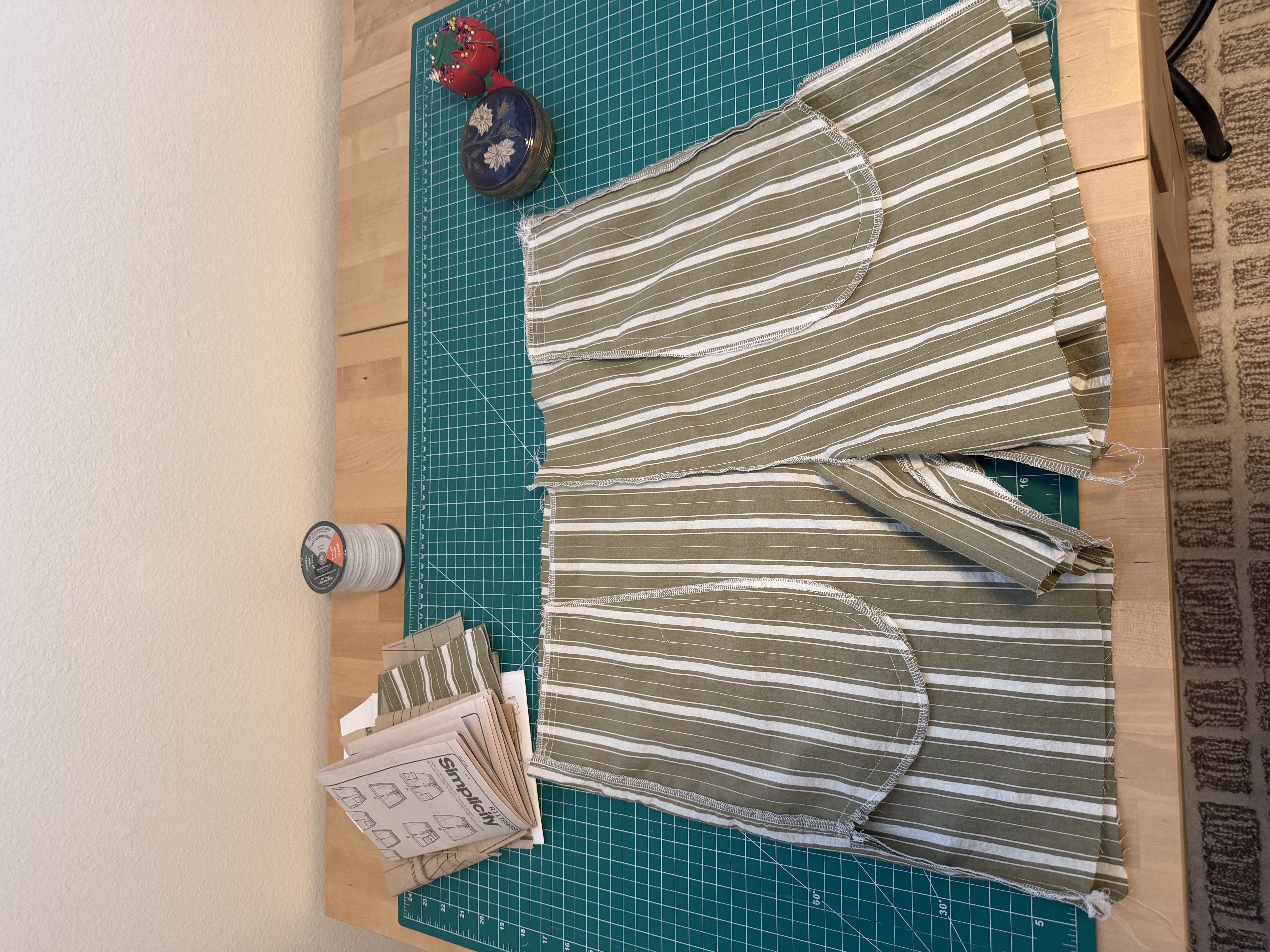 Cut striped fabric pieces and rounded pocket pieces laid out next to the Simplicity S9795 pattern instructions